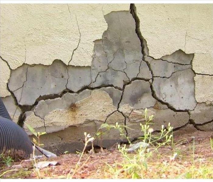  A large and splintering crack in the foundation of a home with someone inspecting it from off picture.